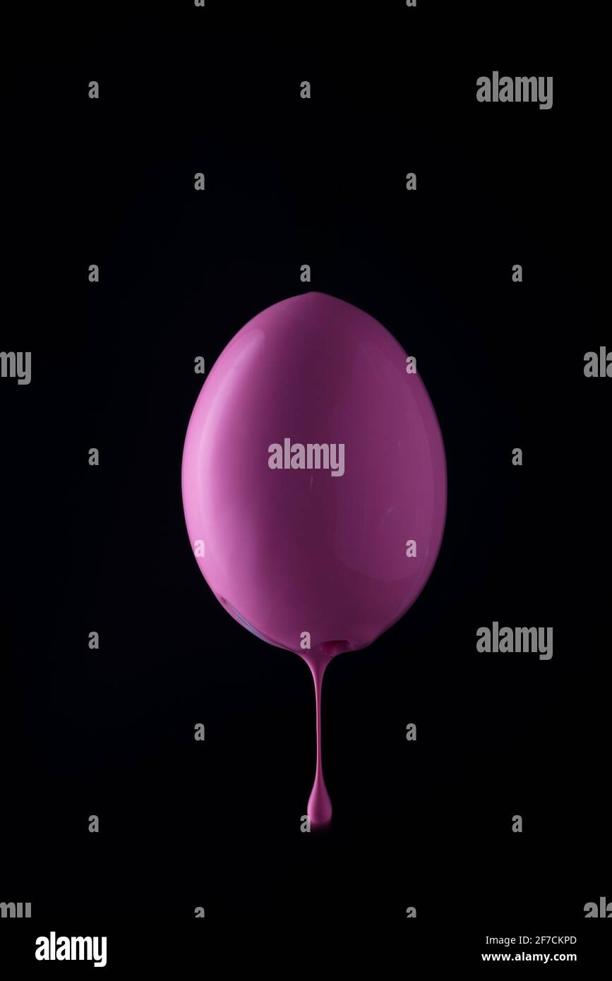 pink egg with paint dripping down. on a black background. minimalistic easter egg close up. Stock Photo