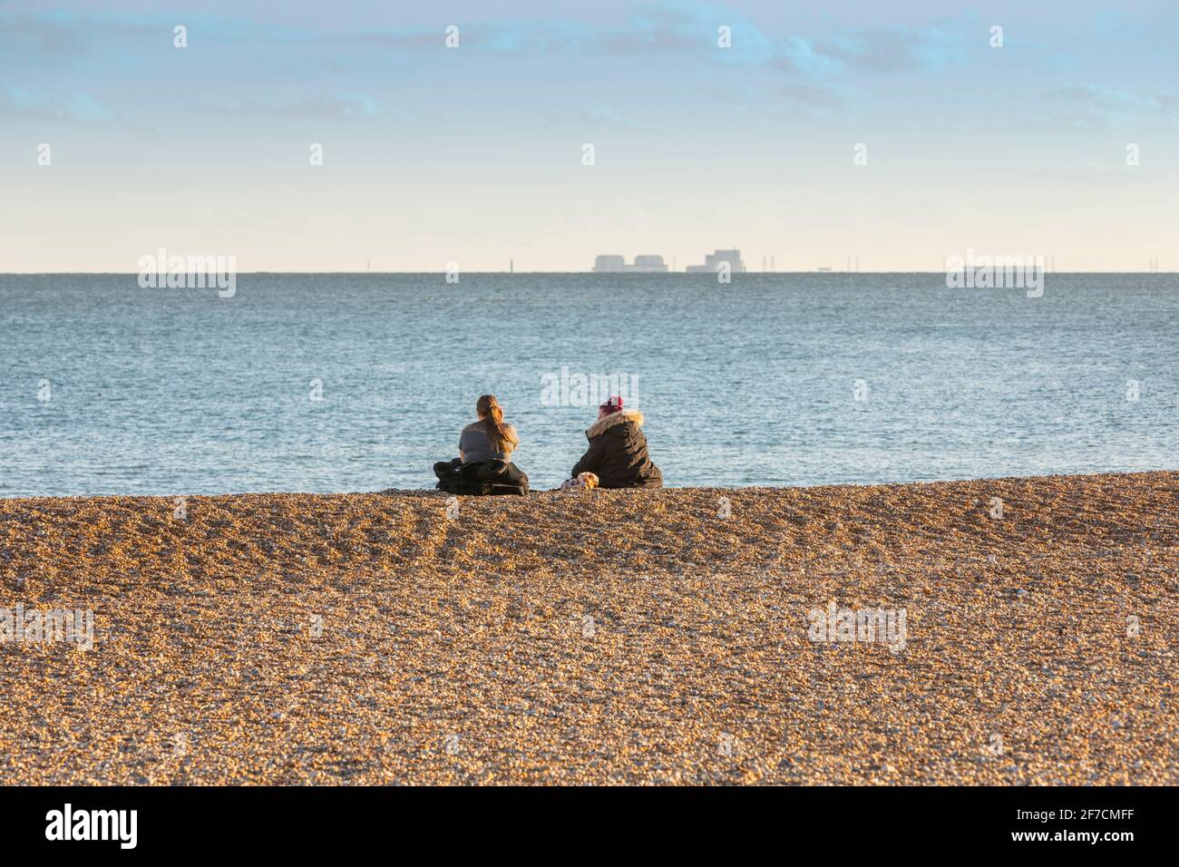 Two young women alone on a shingle beach during covid lockdown Stock Photo