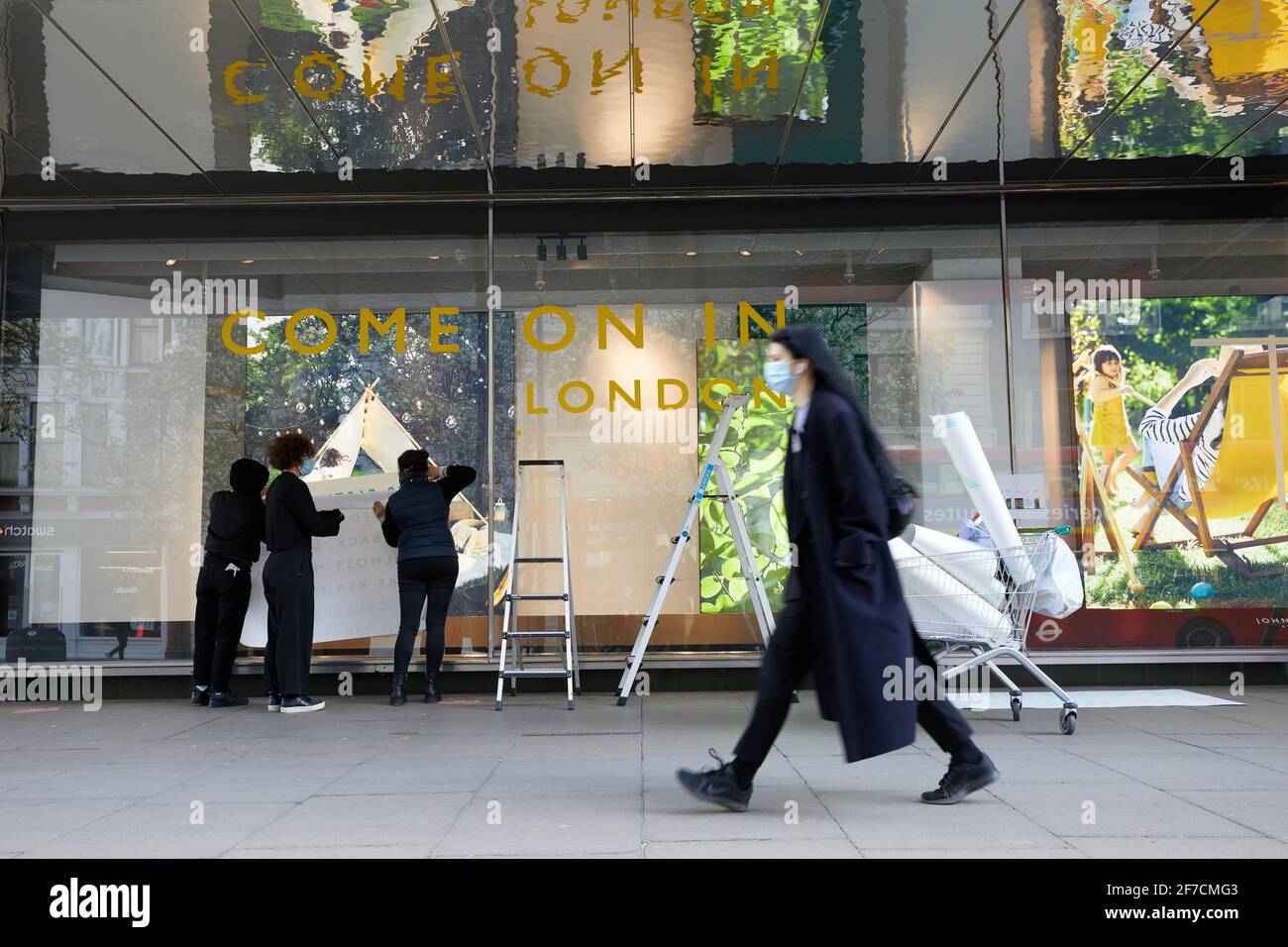 London, UK - 6 Apr 2021: Employees at the John Lewis store on Oxford Street affix signs welcoming shoppers back in advance of lockdown roadmap rules in England that allow shops to reopen on 12 April. Stock Photo
