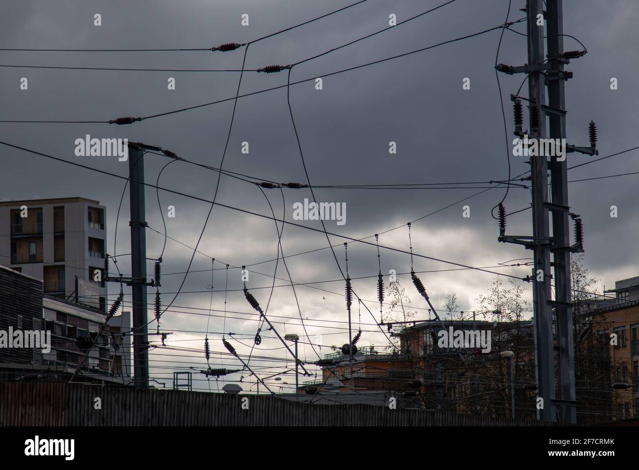 Overhead power lines, including OLE masts, catenary and contact wires, for trains silhouetted against a grey cloudy sky. Stock Photo