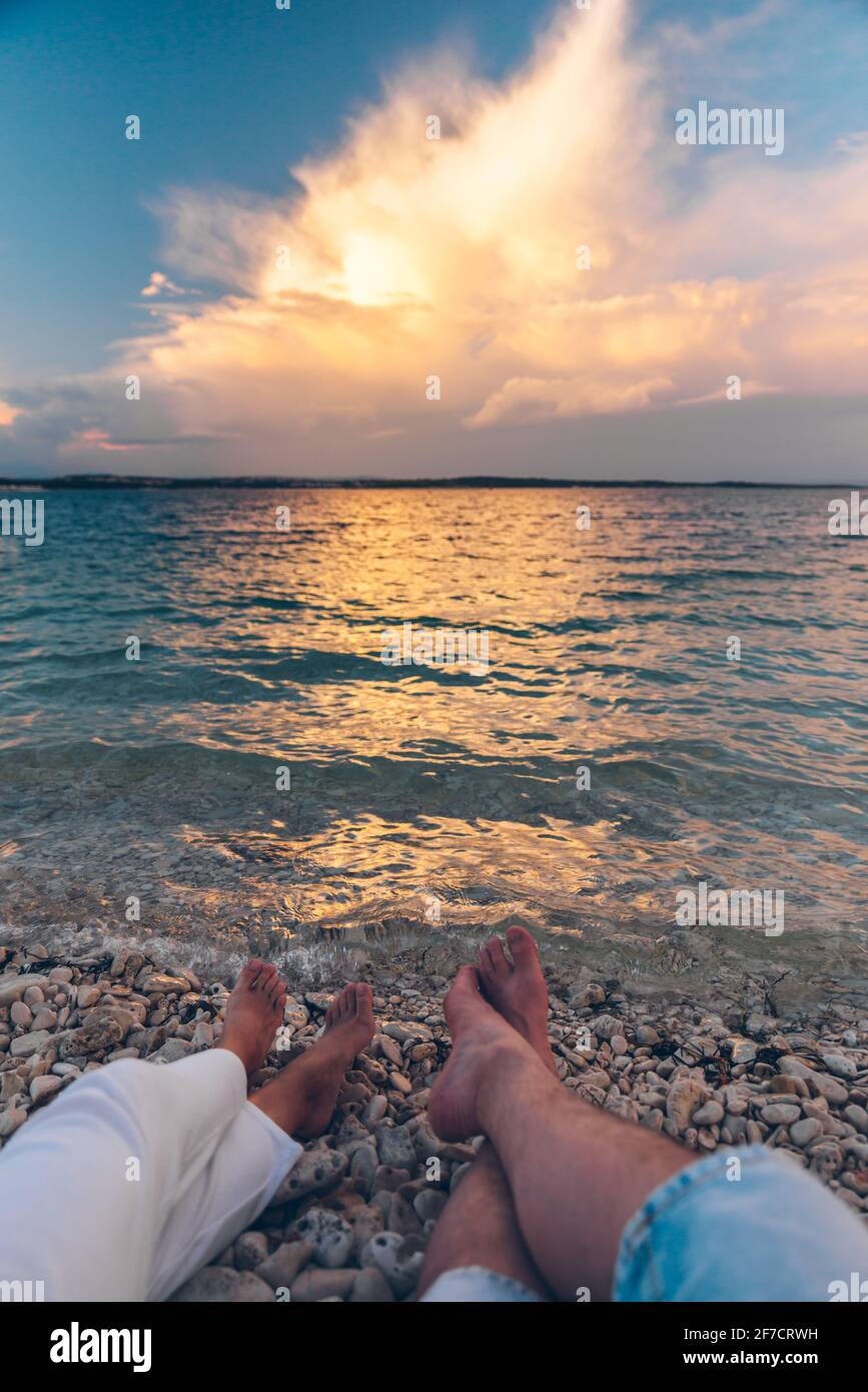 couple laying at the beach looking on sunset above sea. body parts legs ...