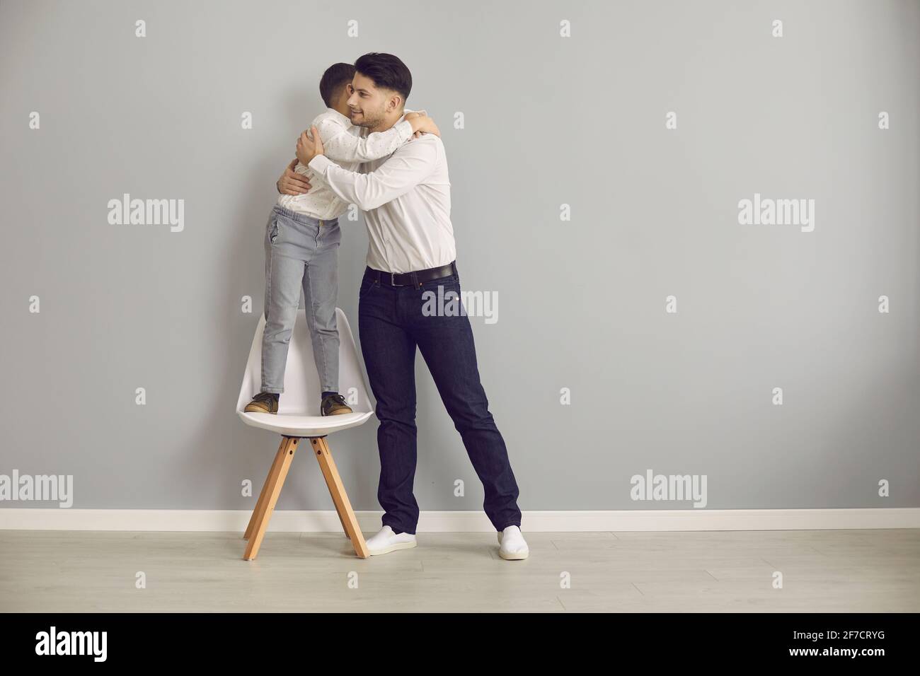 Loving father tightly hugging adorable son standing on chair studio portrait Stock Photo