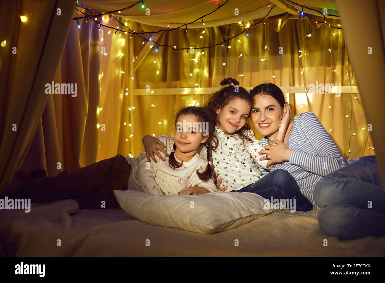 Happy mother and daughter children hugging sitting together in tent home Stock Photo