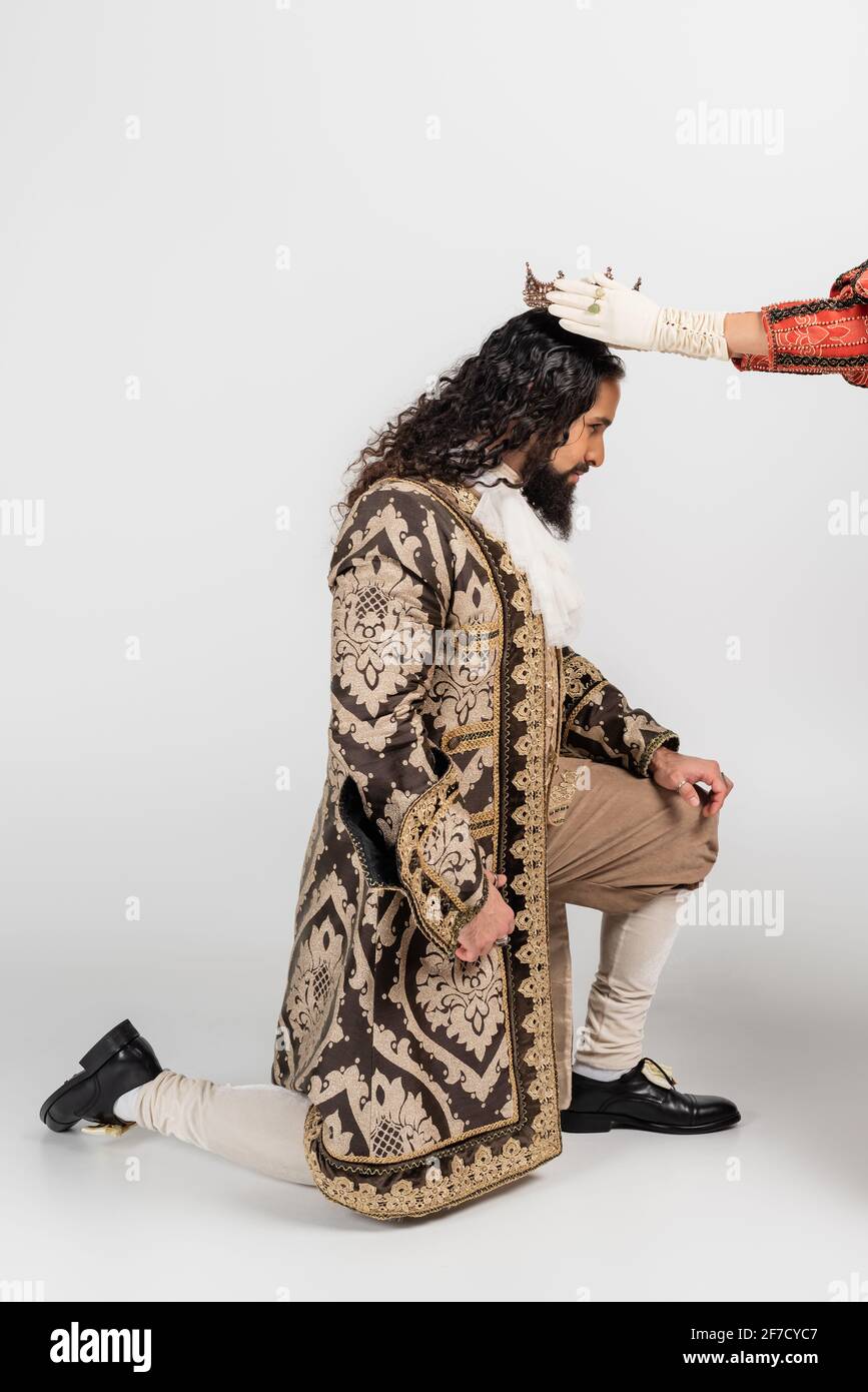 queen wearing crown on hispanic king in medieval clothing standing on knee on white Stock Photo
