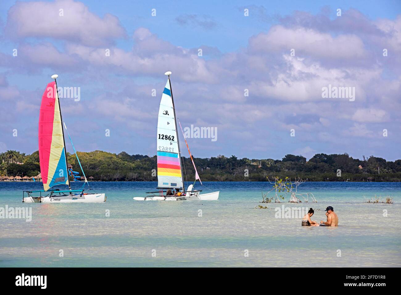 Tourists sitting in shallow water and two sailboats / catamarans sailing on Lake Bacalar / Laguna de Bacalar, Quintana Roo, Yucatán, Mexico Stock Photo