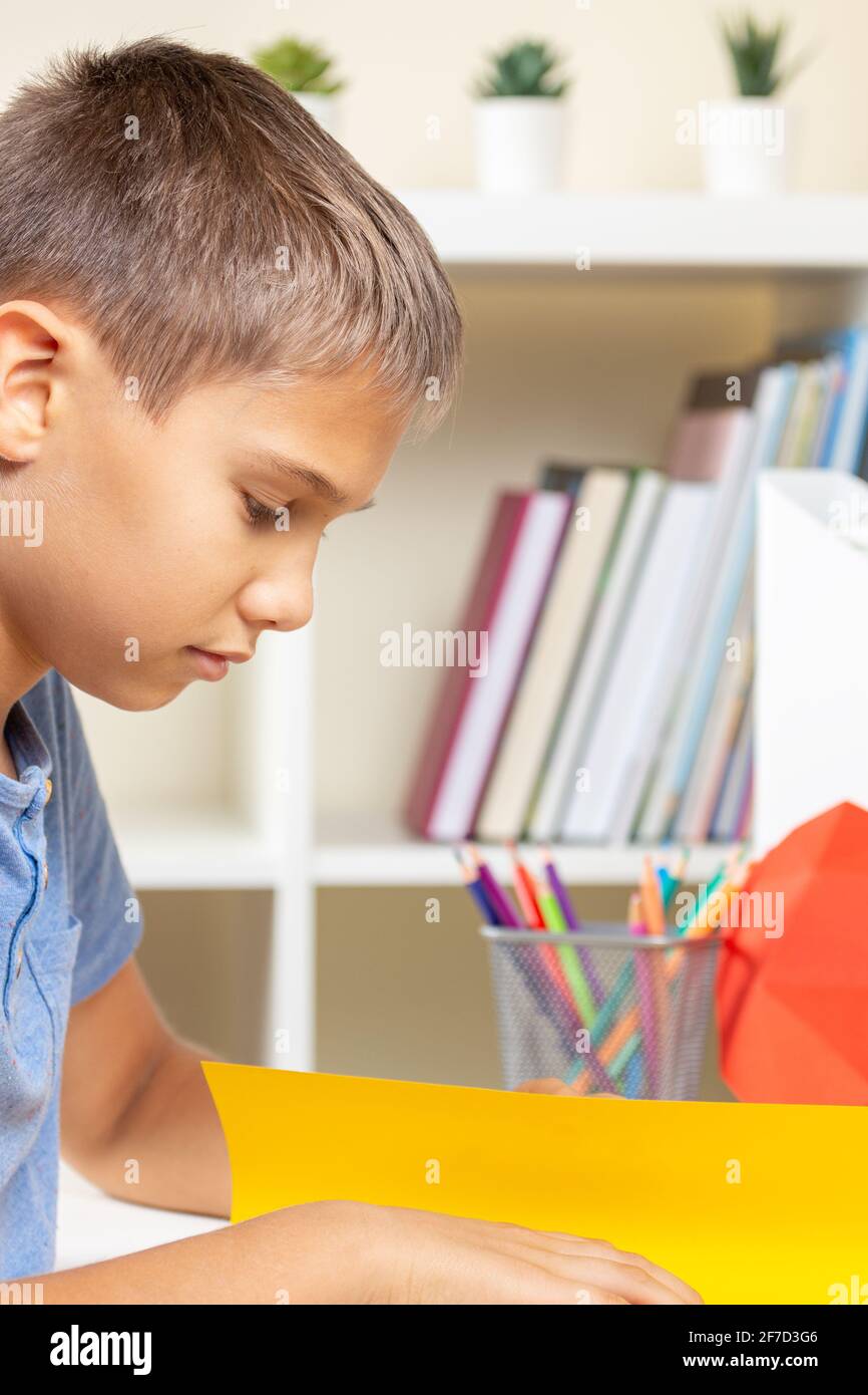 Kid create origami colored paper card white watching video tutorial on tablet computer. Education, learning, paper craft, entertainment at home Stock Photo