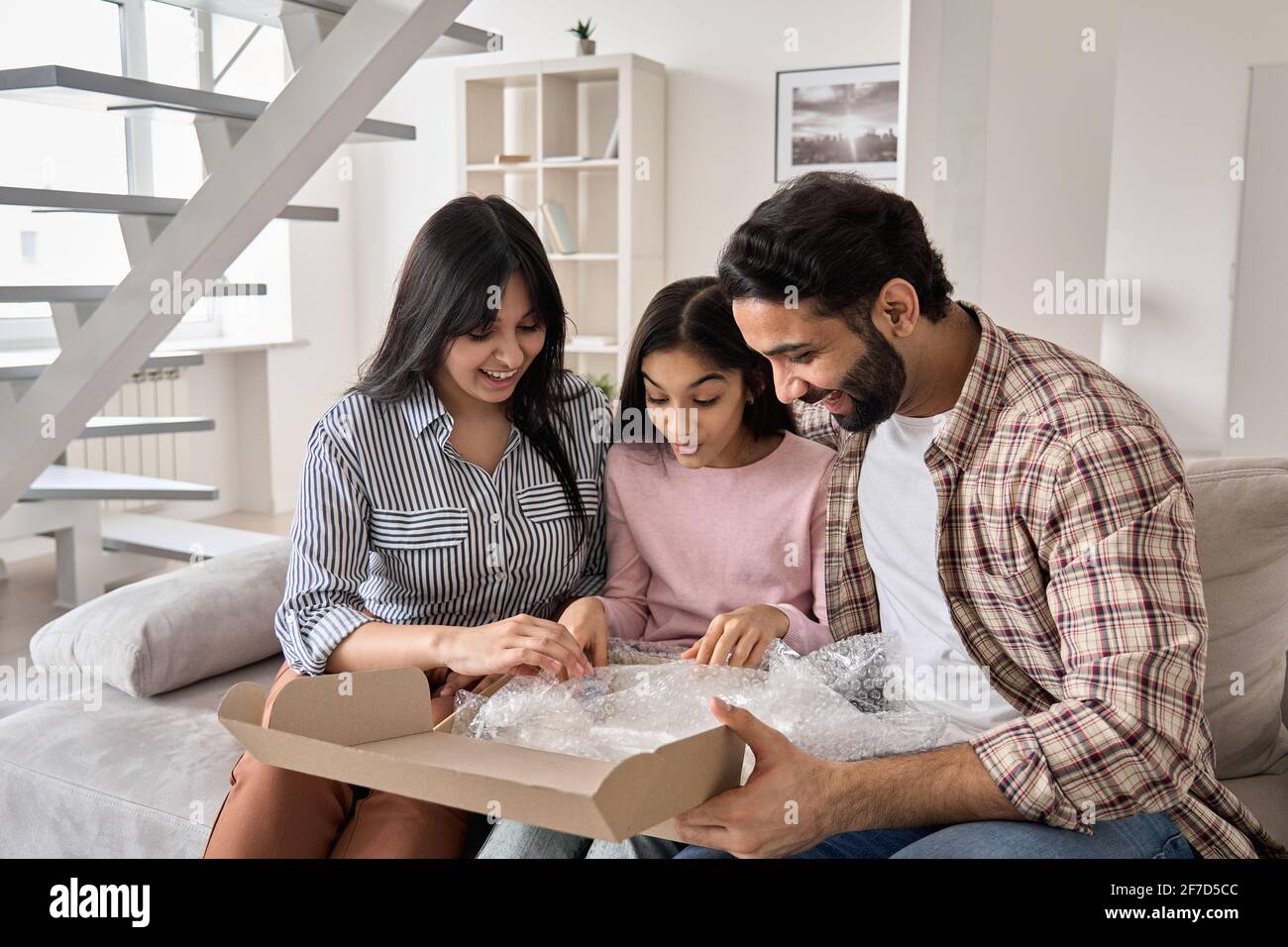 Excited indian family with teen daughter unpacking parcel at home. Stock Photo