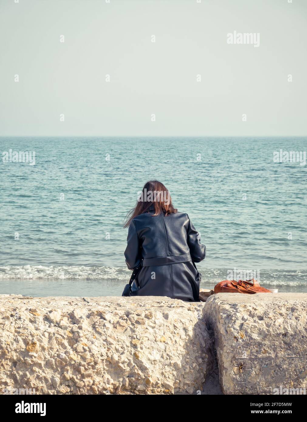 Girl sitting on a rock on the beach of the Black Sea and looking at the ...