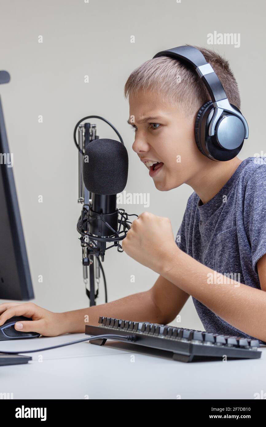 Teenage boy wearing headphones using microphone and looking to computer ...
