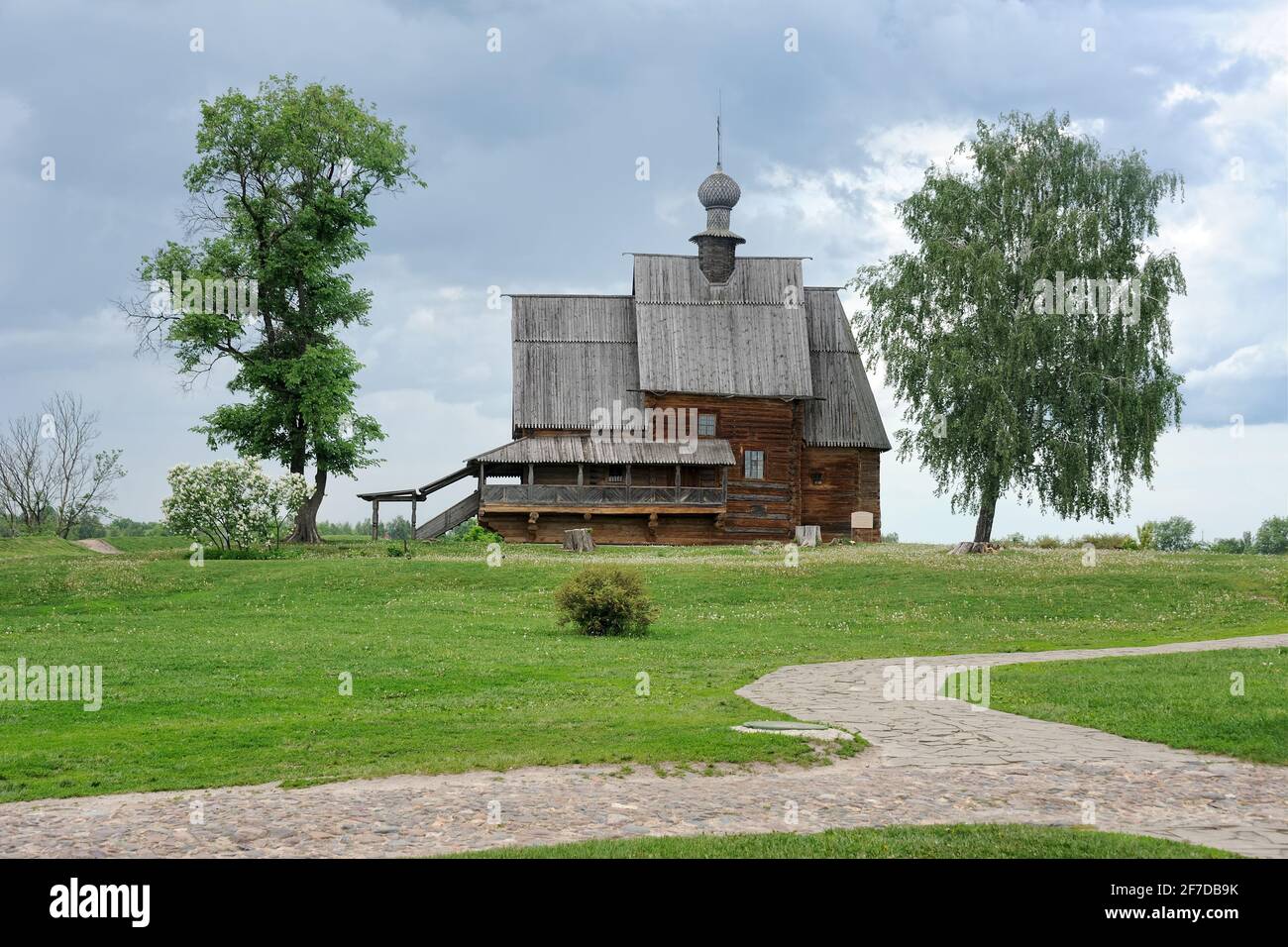 = Wooden Church Framed by Trees Under Gray Clouds =  Old wooden church of St. Nicholas on the grounds of Suzdal’s Kremlin framed by trees under gray c Stock Photo