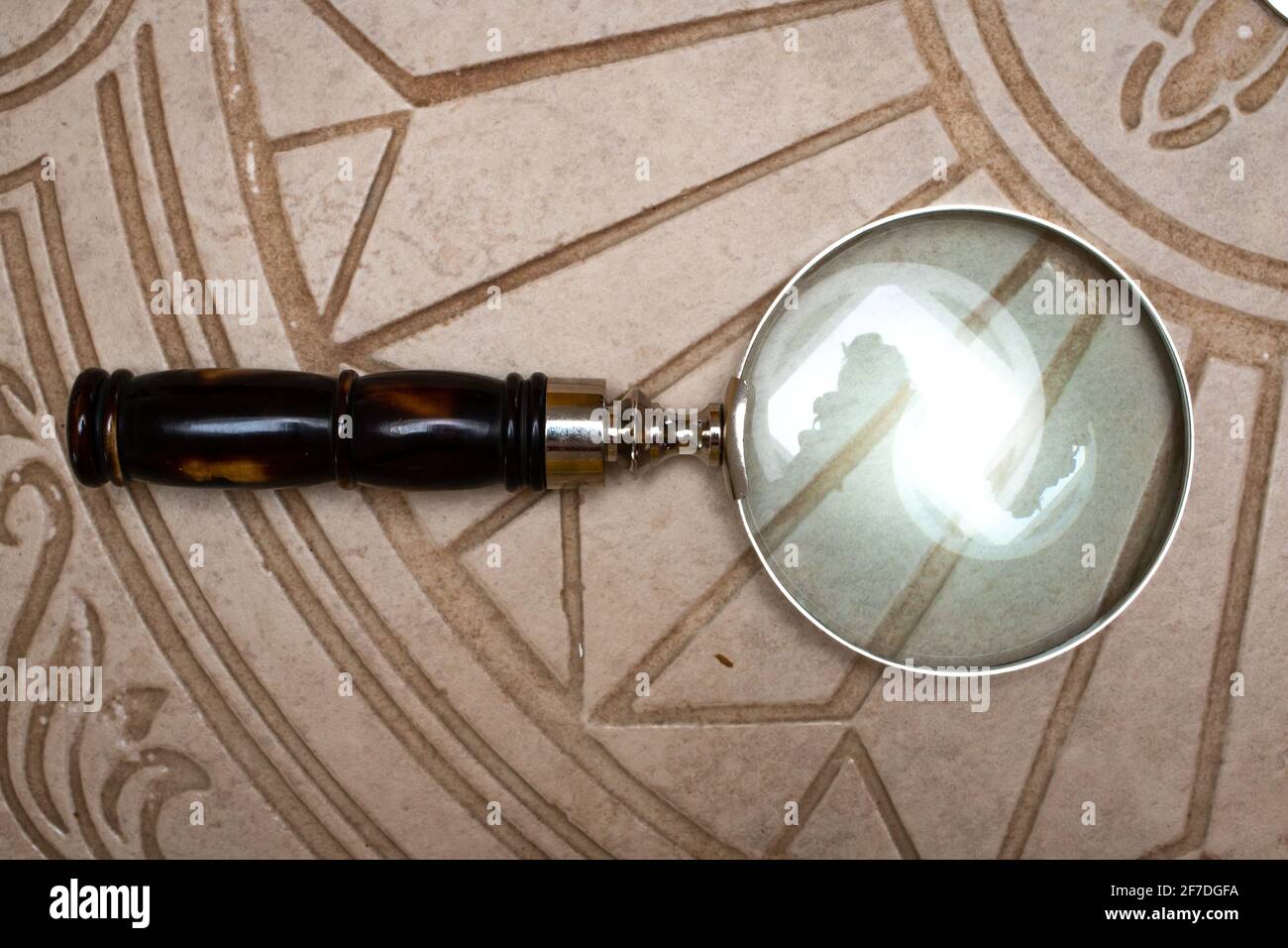 Vintage magnifying glass on intricate beige tile. Stock Photo