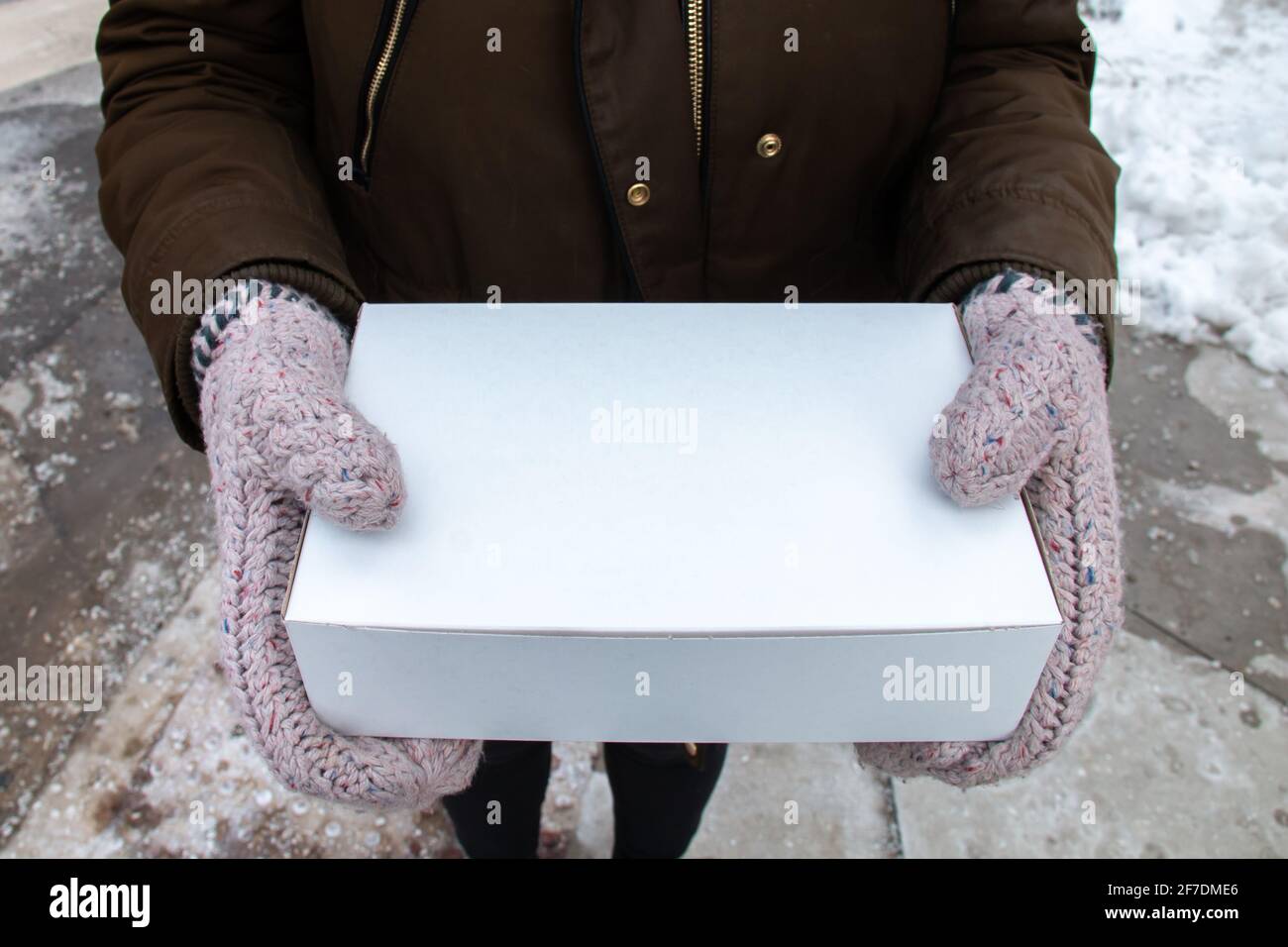 Woman holding a box of donuts in London, Ontario, Canada during February 2021. Photo includes blank space on the takeaway container for logos. Stock Photo