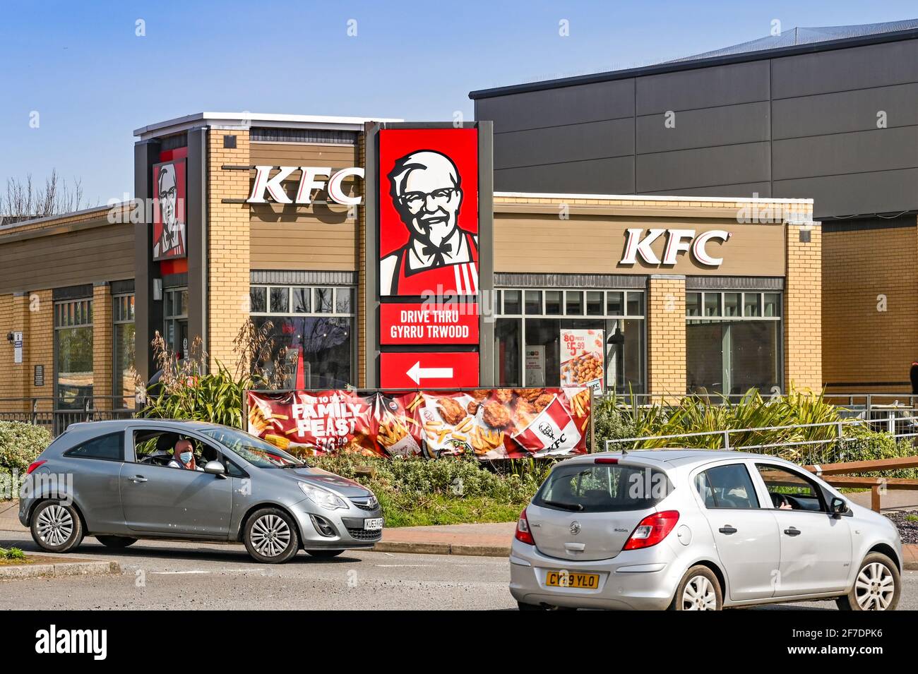 Barry, Wales - March 2021: Cars driving past the outside of a branch of KFC. A sign is point the way to the drive thru point. Stock Photo