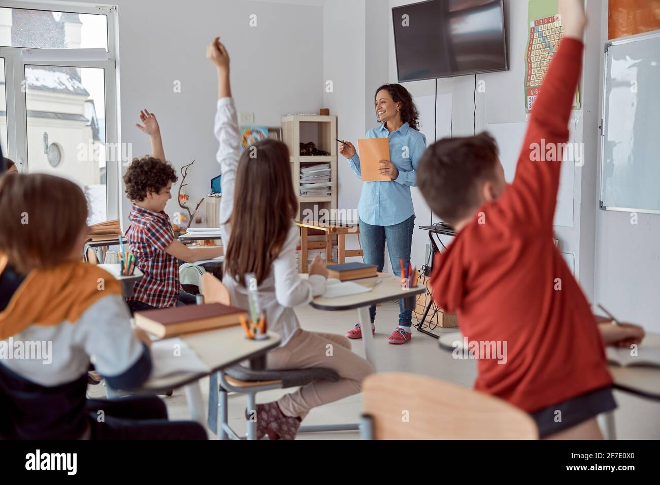 School children sitting at the desk in classroom and raising hands ...