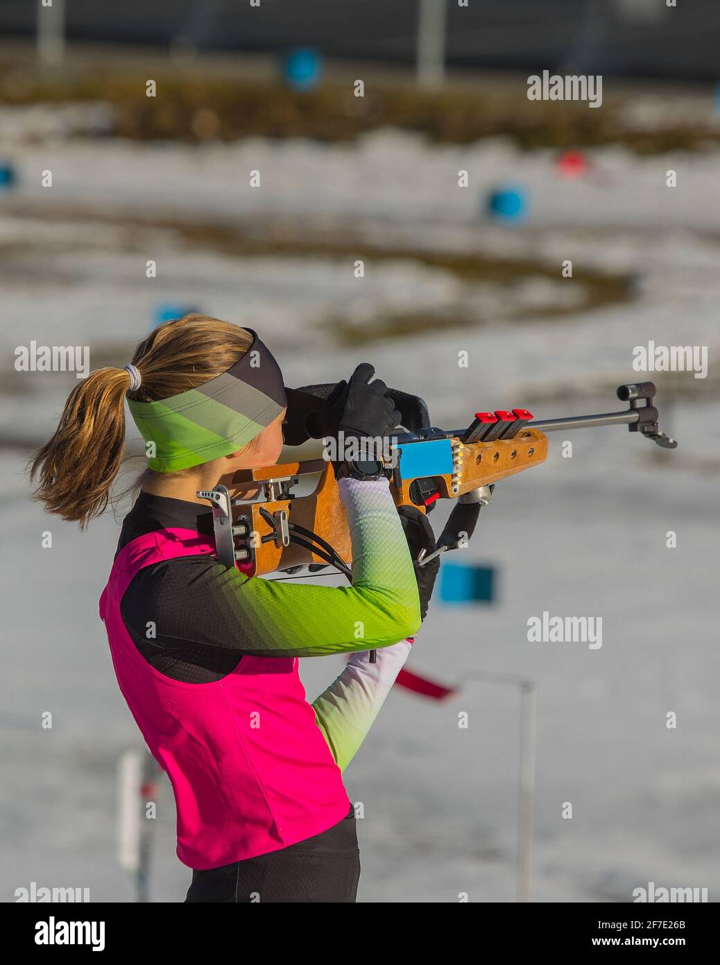 Female biathlon racer is standing on the ground and aiming her rifle