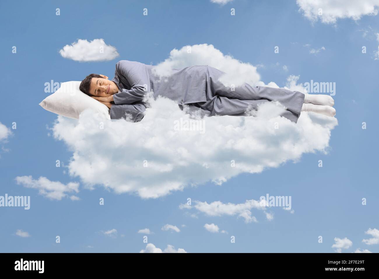 Man in pajamas sleeping on a cloud and floating in the sky Stock