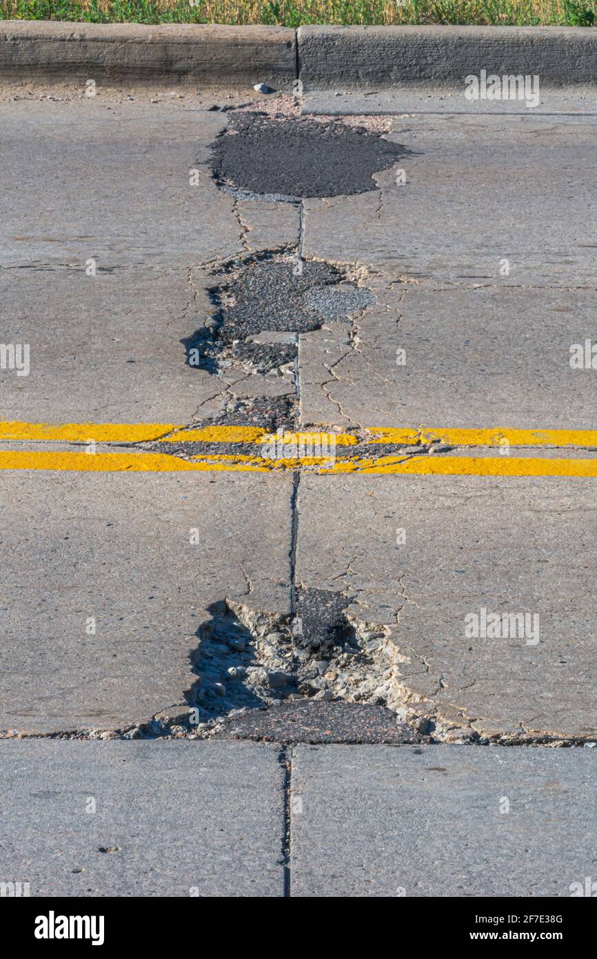 Old worn concrete road highway pavement in disrepair showing cracks, patches, repairs and chuck holes, Castle Rock Colorado USA. Photo taken in July. Stock Photo