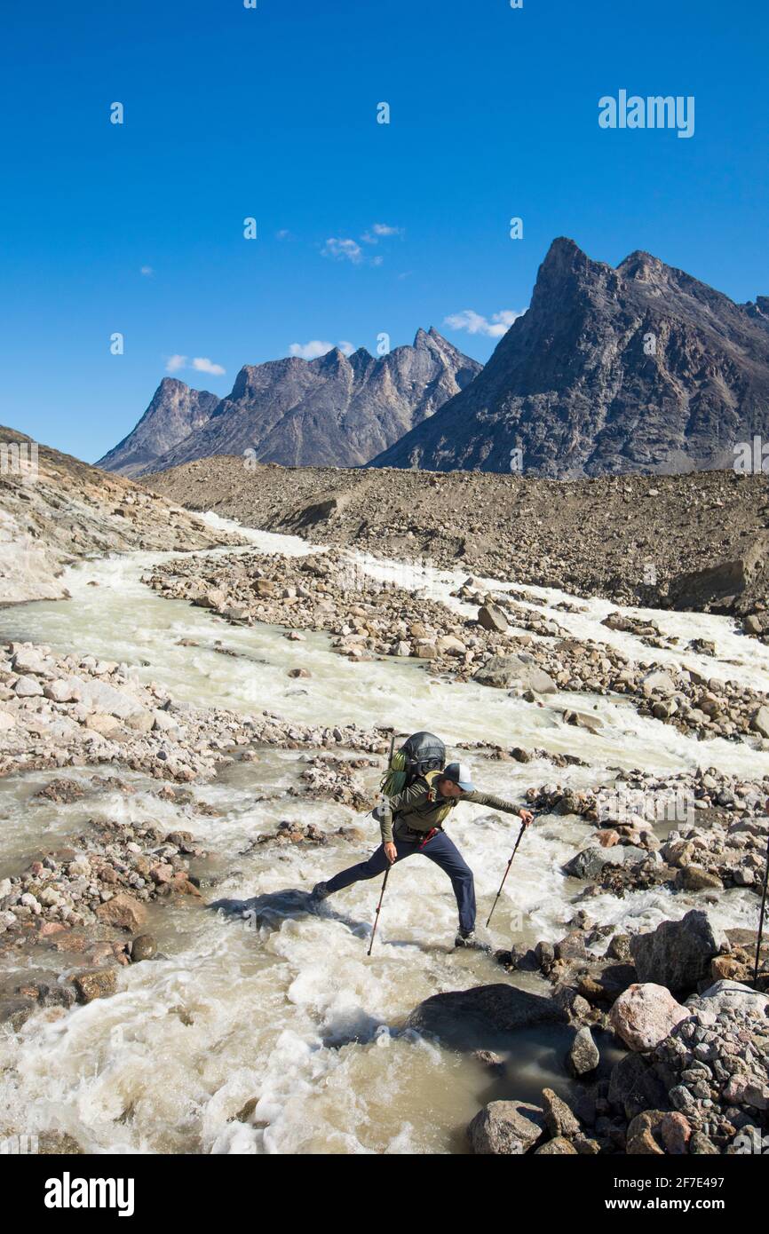 Backpacker steps across a raging river, Akshayak Pass. Stock Photo