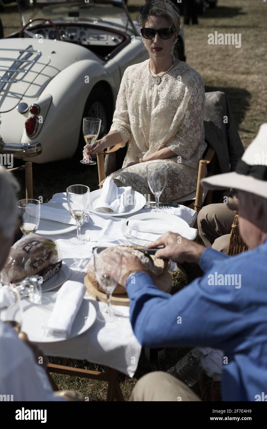 A woman and a man having a picnic at Goodwood Revival surrounded by classic cars , Chichester, West Sussex, England Stock Photo