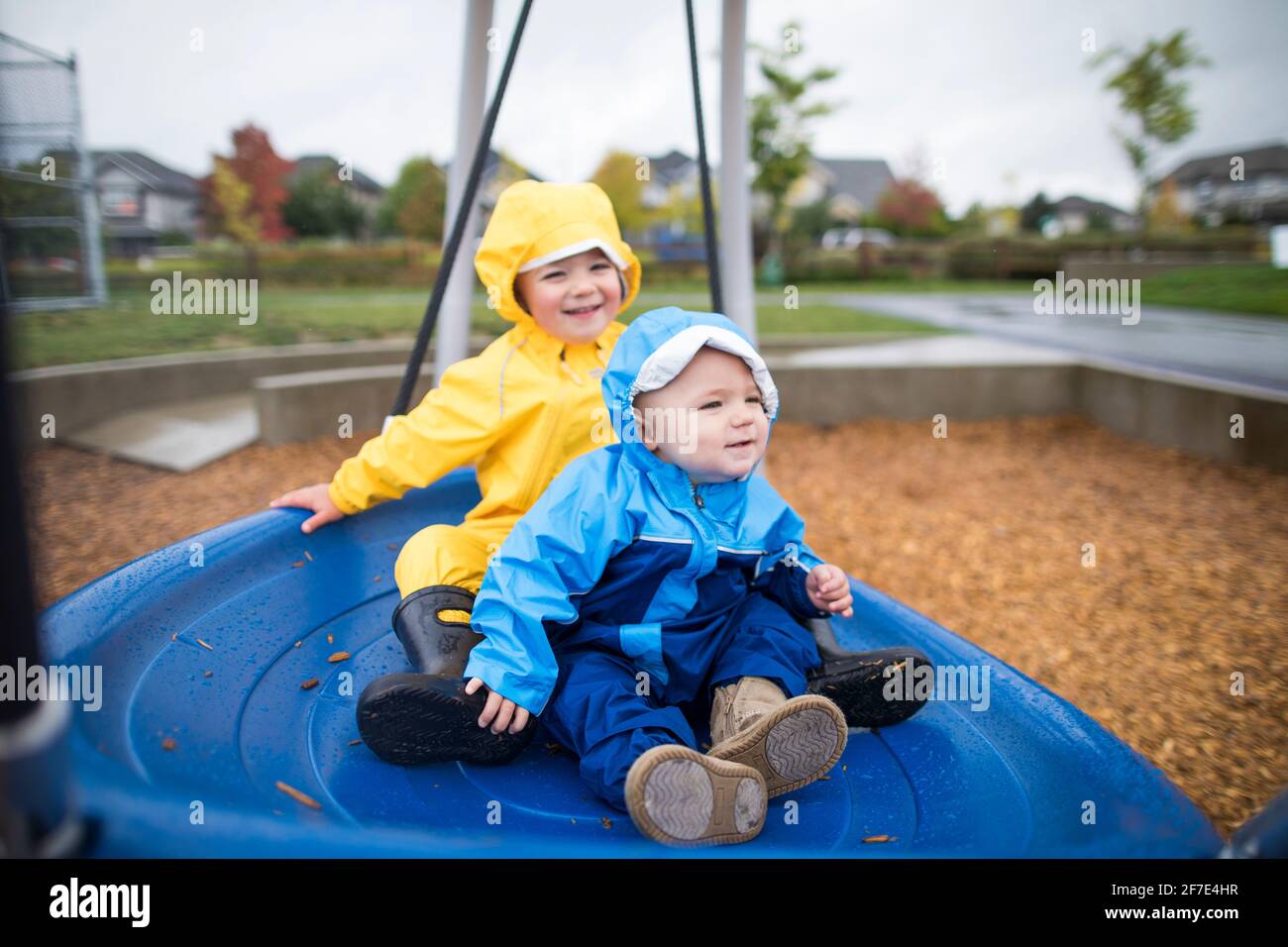 Two kids sit on a large blue swing at the park Stock Photo