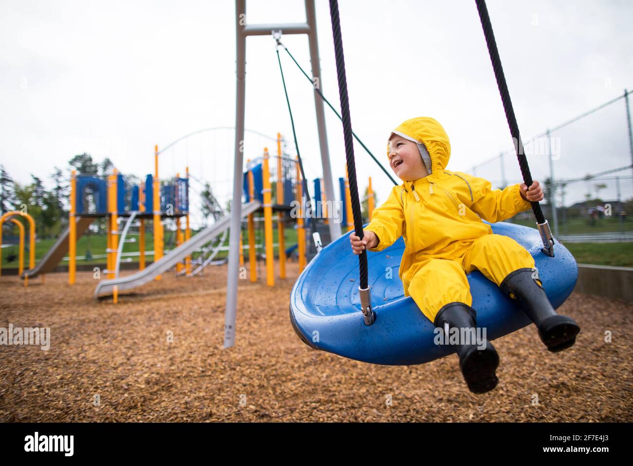 Happy toddler boy rides on swing at the park on a wet day Stock Photo