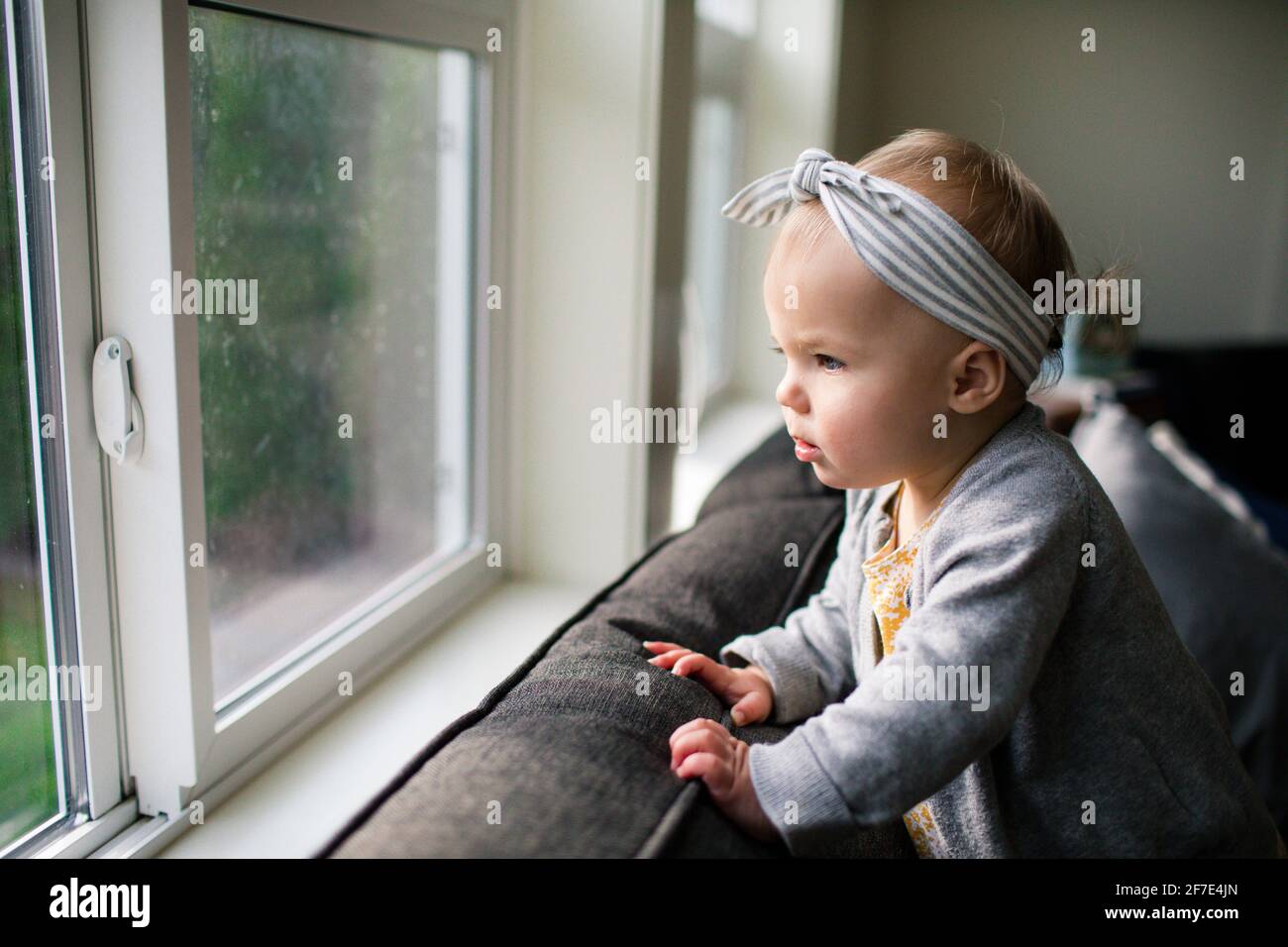 Pretty young girl looking out window from inside her home. Stock Photo