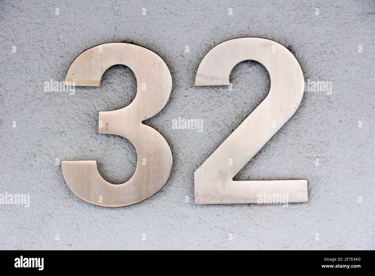 Number 32 in stainless steel on a white plaster wall Stock Photo