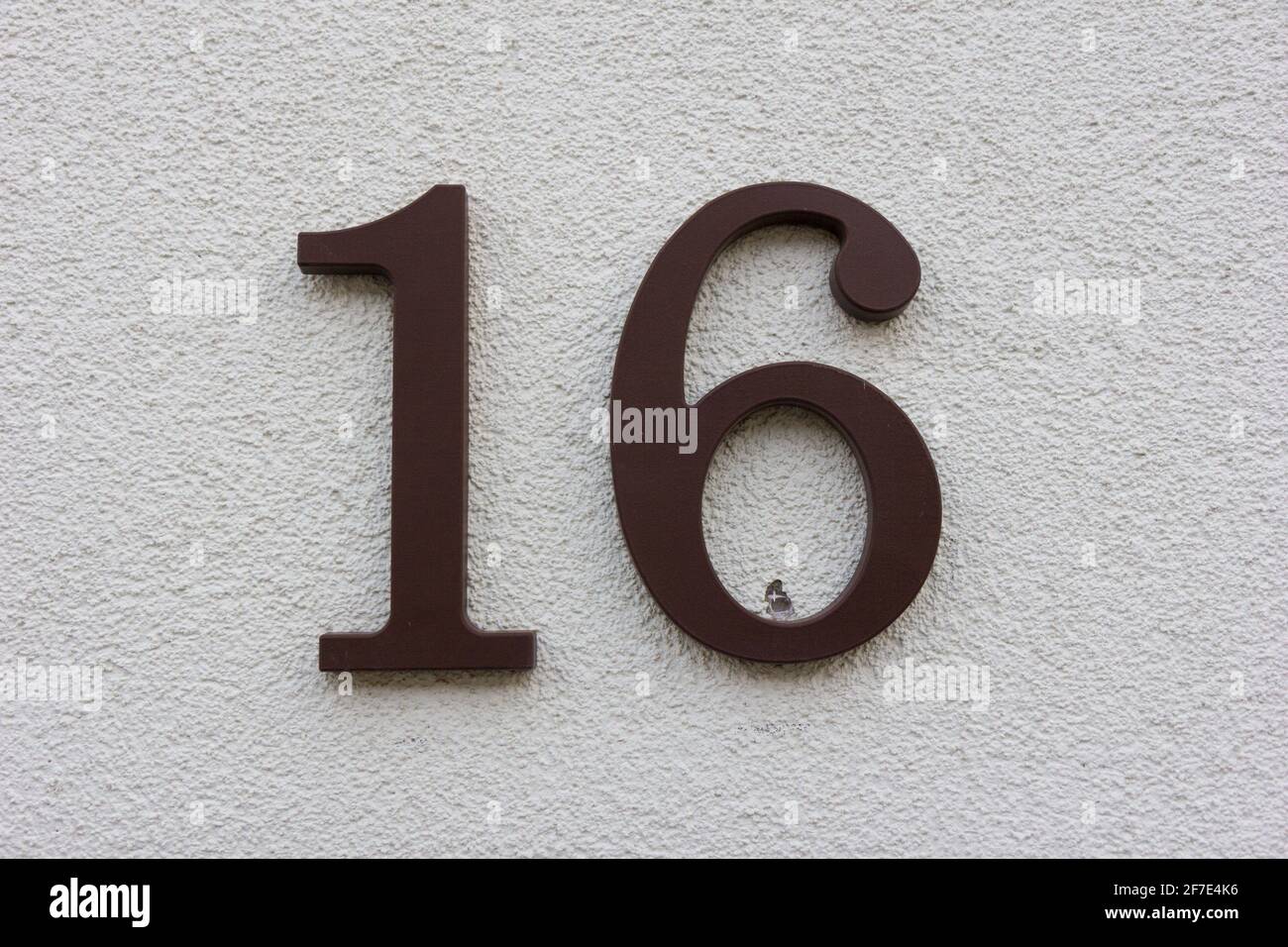 Number 16 in brown plastic on a white plaster wall Stock Photo