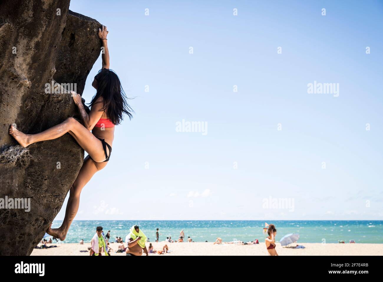 Tenacious woman scaling to the top of the giant rock at Waimea bay Stock Photo