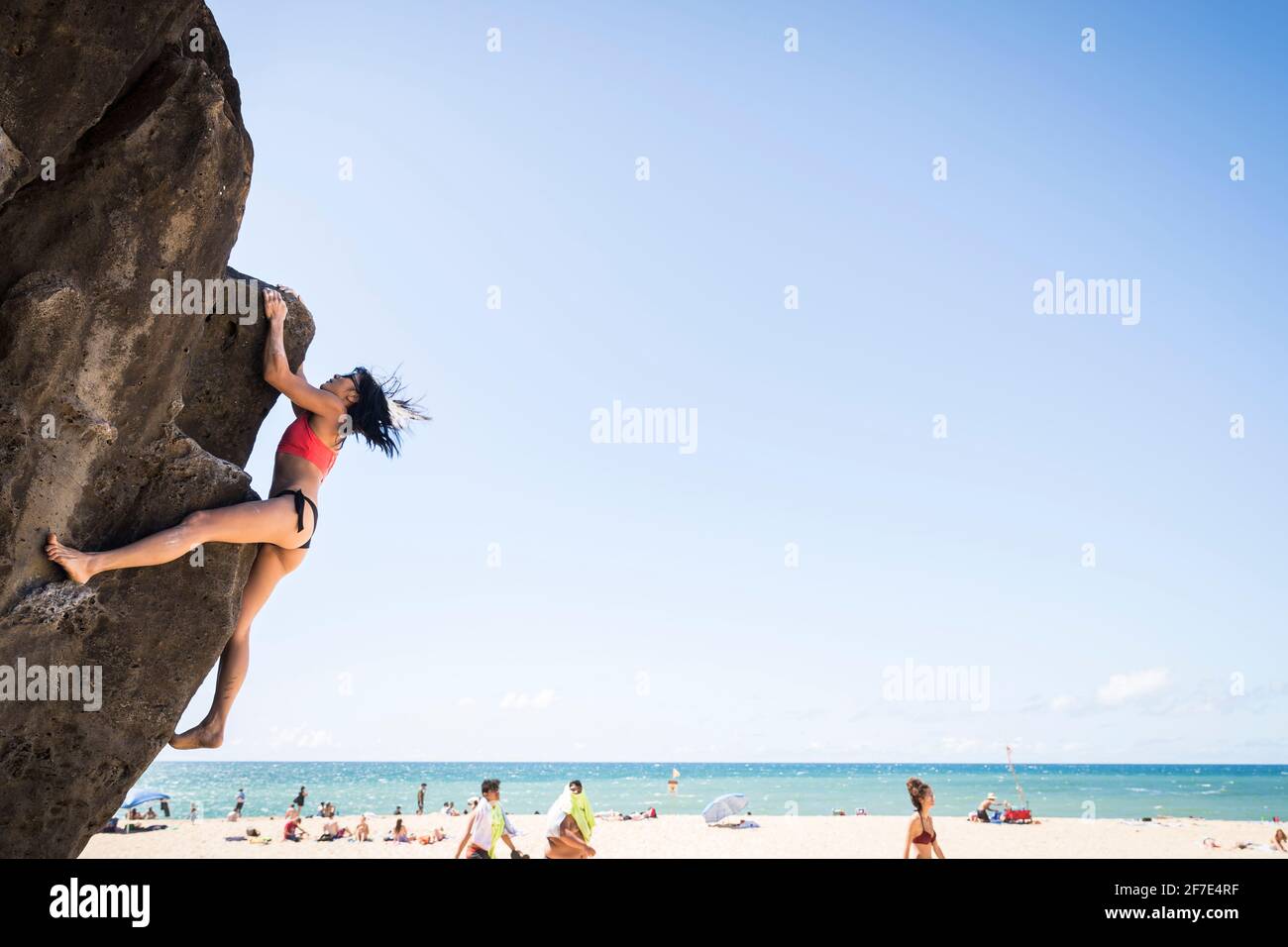 Daring lady scaling a boulder with no harness on a sunny beach in Oahu Stock Photo