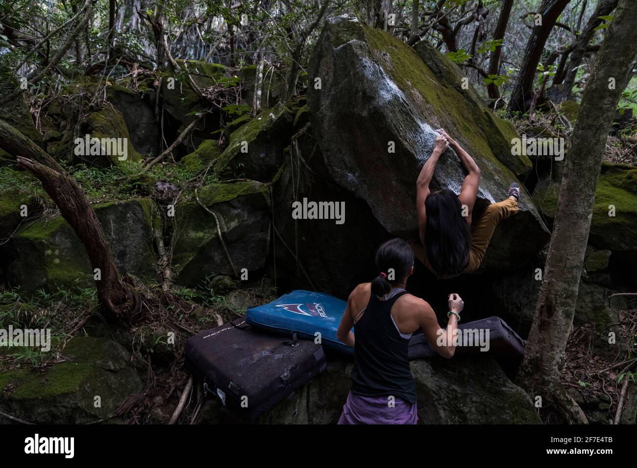 Two athletic women taking turns bouldering a mossy rock in Oahu Stock Photo