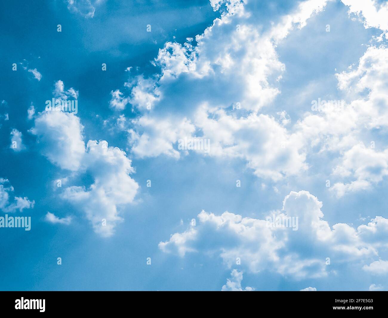 background of Summer sky of fluffy clouds, sun shining and moving clouds with copy space. Stock Photo