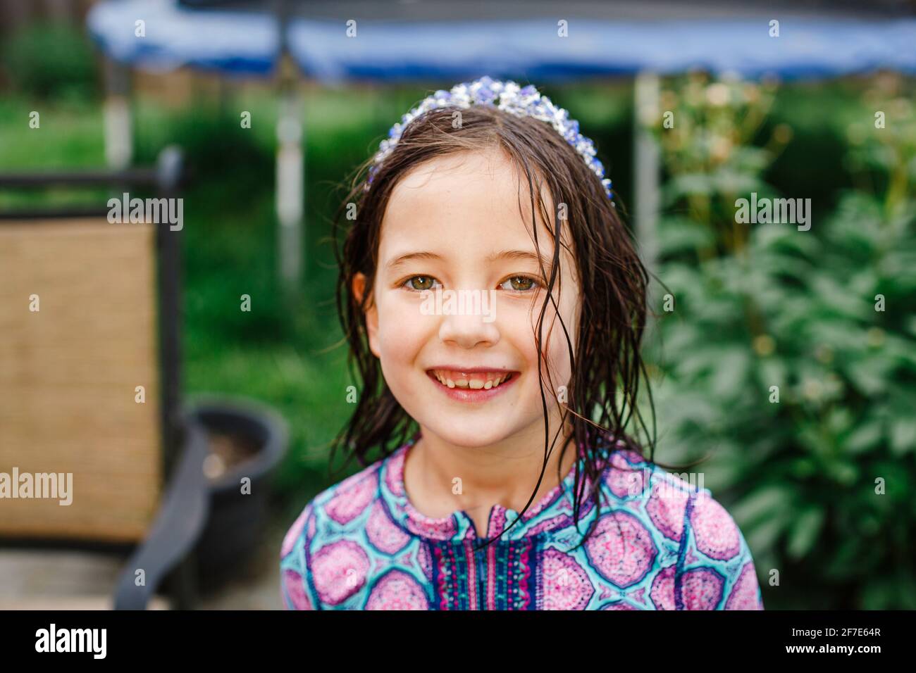 A smiling child stands with direct gaze, wet hair, and a purple crown Stock Photo