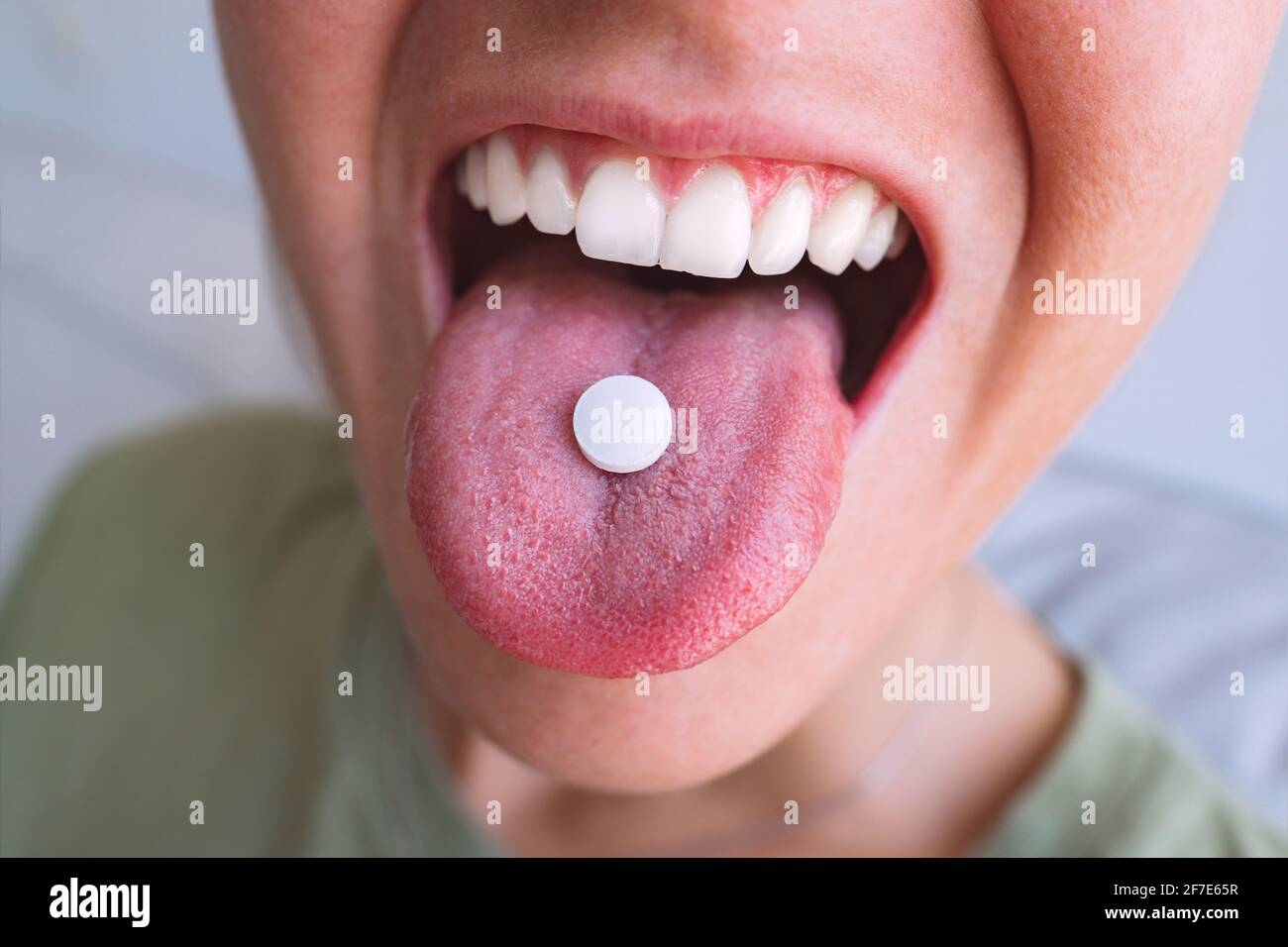Young woman taking pill. Closeup of white round pill on tongue. Open mouth holding tablet Stock Photo