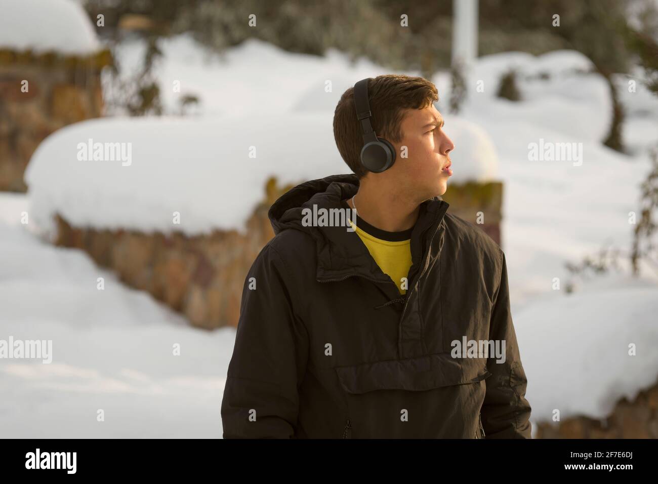 Blue-eyed millennial boy with coat listening to music on headphones Stock Photo
