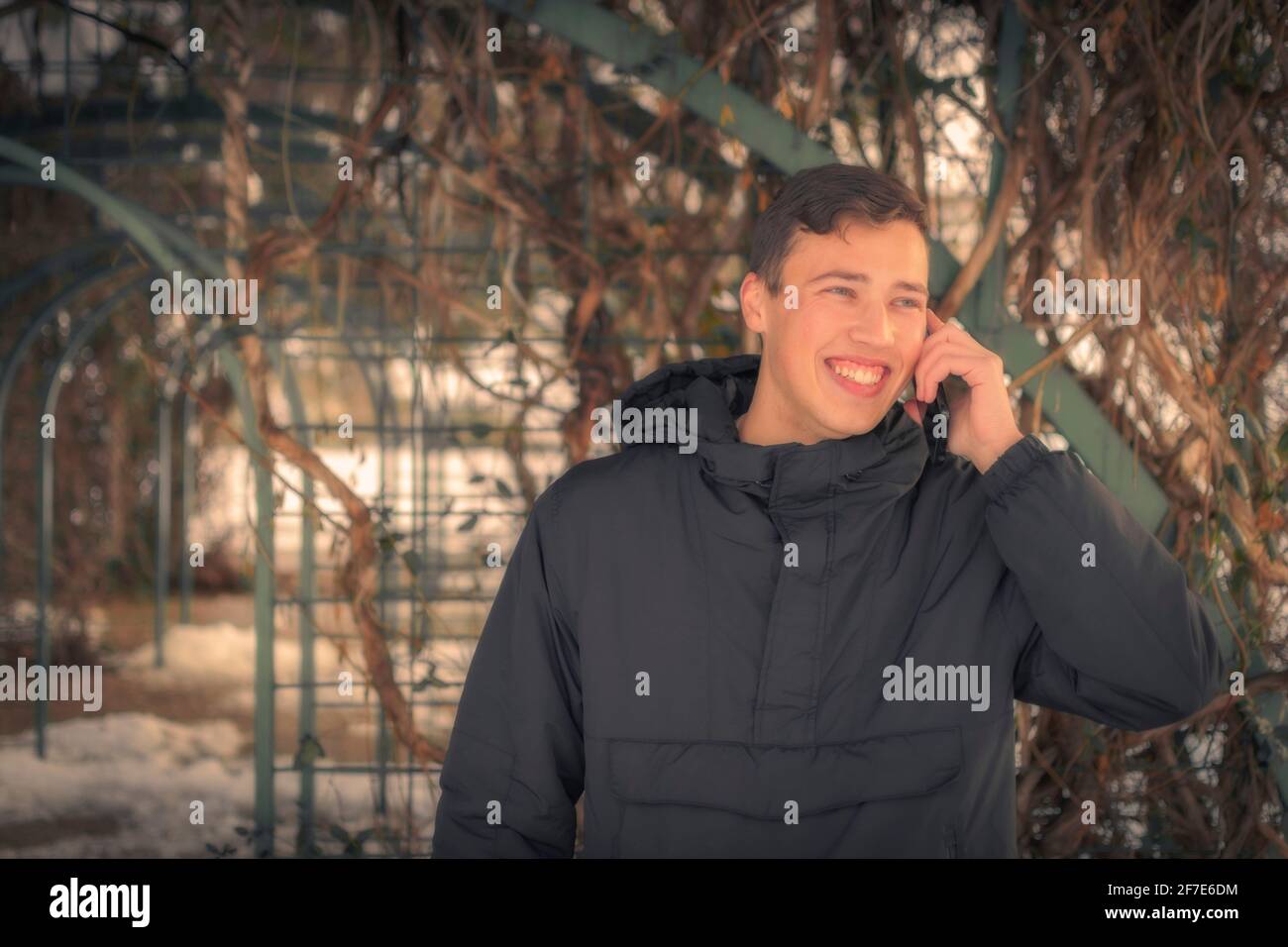 Blue-eyed college boy smiling while talking on mobile phone at garden Stock Photo