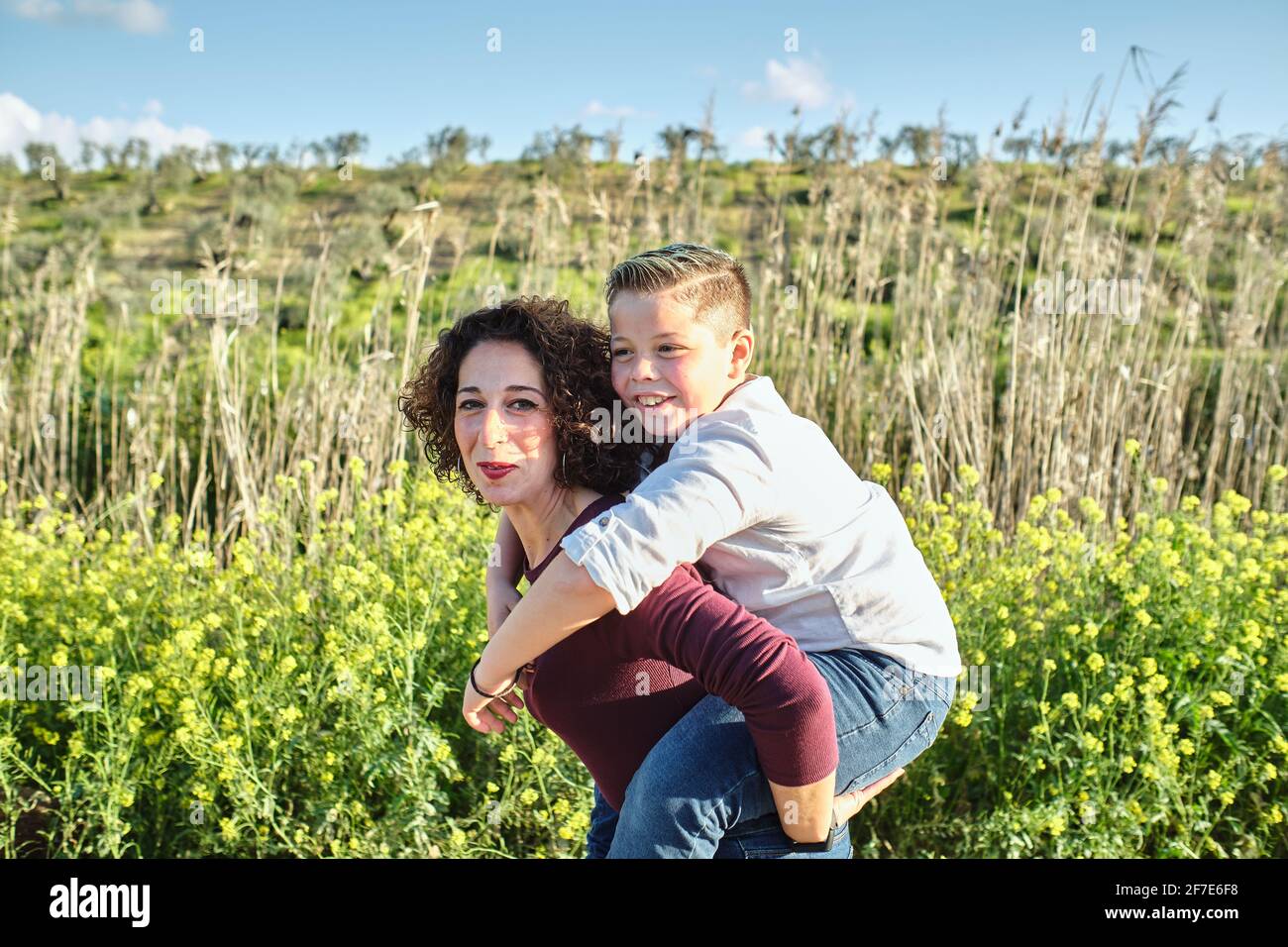 happy mother takes her son on her back and walks him through the field Stock Photo