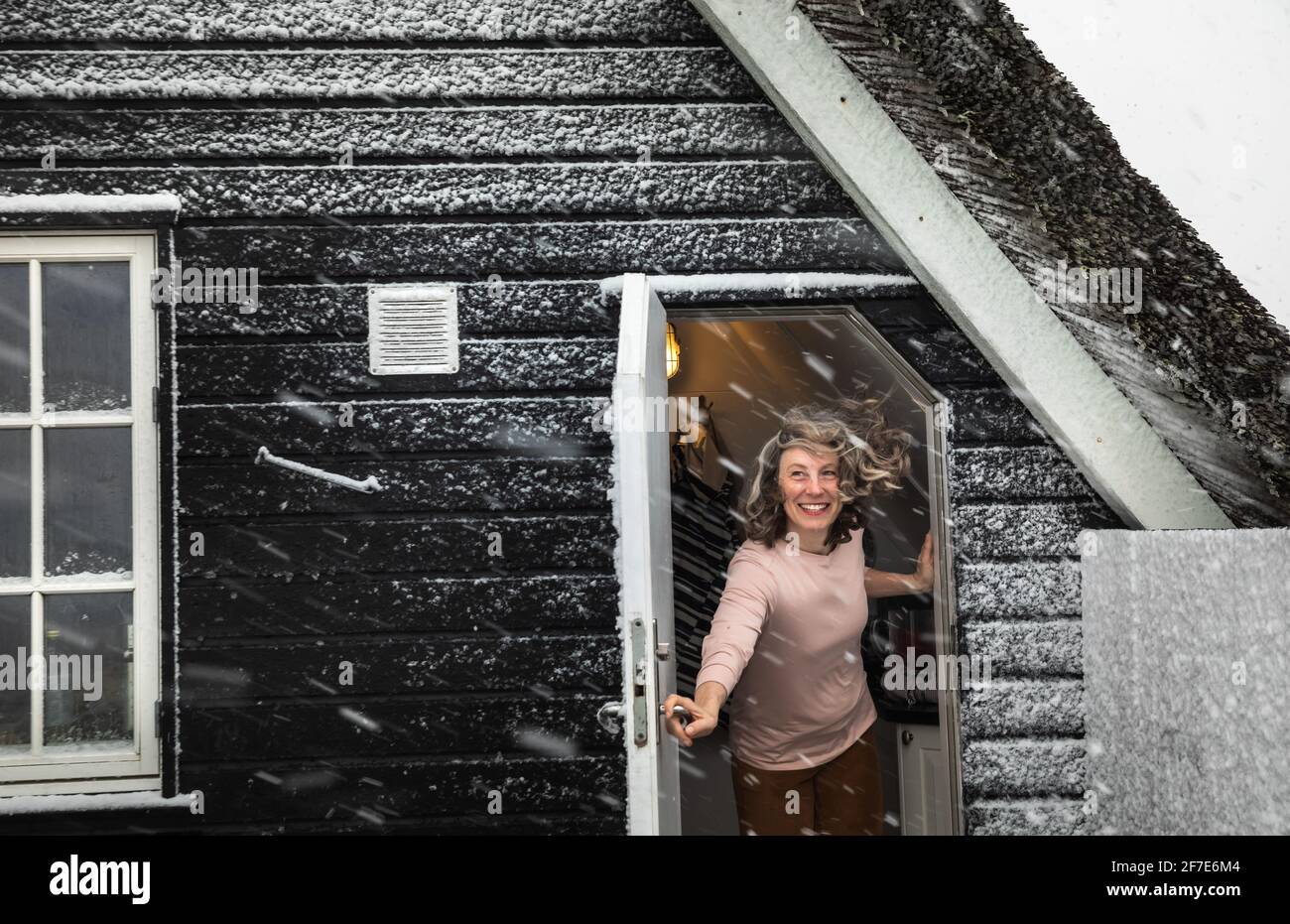 Woman Holding Door Open With Hair Blowing In Snow Storm in Denmark Stock Photo