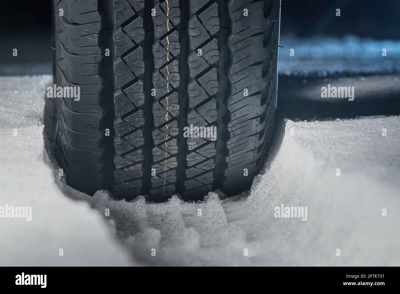 All terrain tire in snow. Snow track visible in snow with a rubber car or SUV tire in front. Tread marks in snow. Winter road safety concept. Stock Photo
