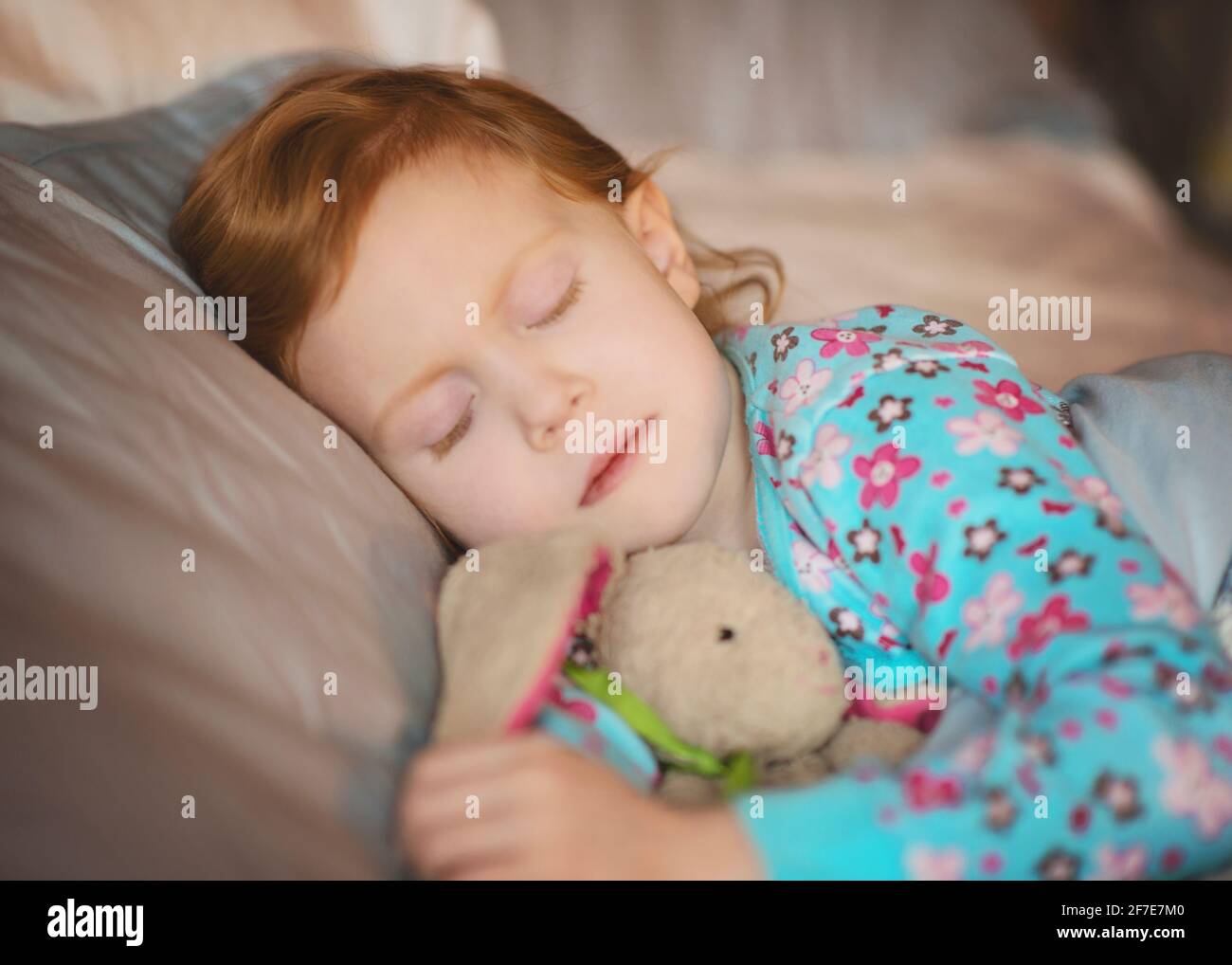 Sweet little red haired girl sleeping with stuffed bunny. Stock Photo