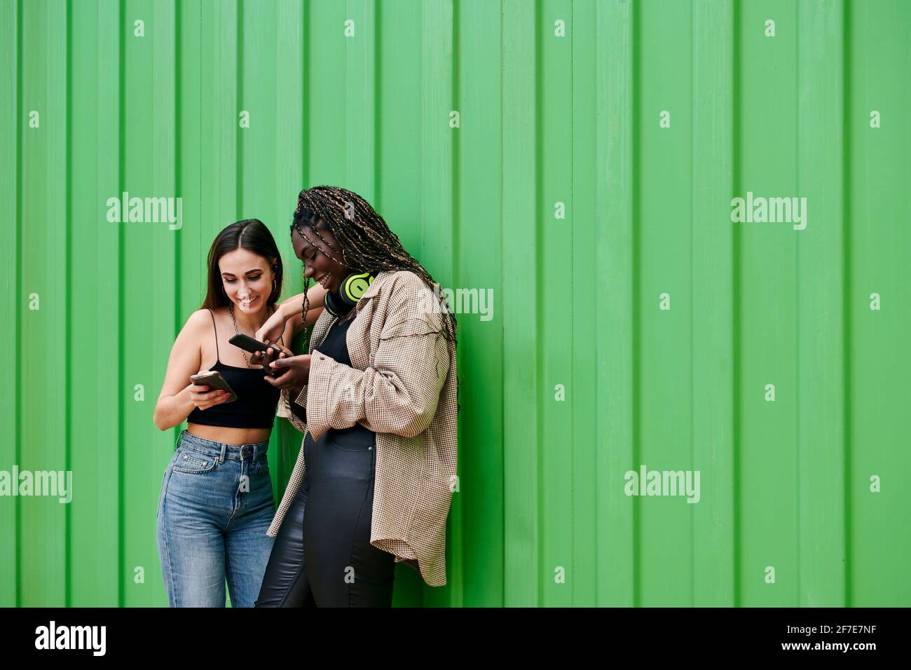 Two young multiethnic women talk, smile and look at their phones Stock Photo