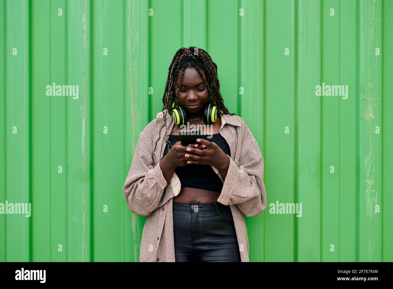 Black woman in urban clothing looks at her mobile while she is smiling Stock Photo