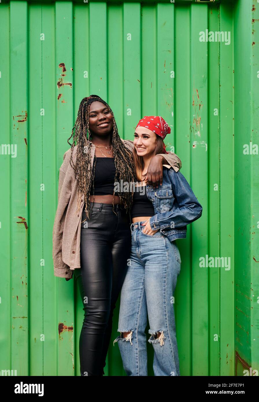 Two multiethnic women in urban clothing smile and hug each other Stock Photo