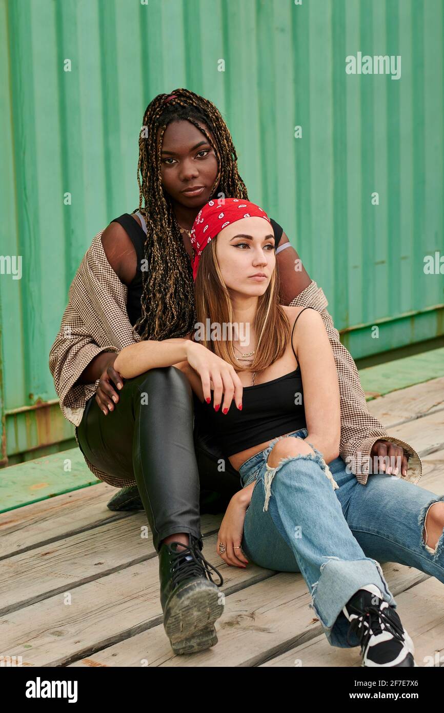 Multiethnic women embracing in urban clothing pose facing the camera Stock Photo