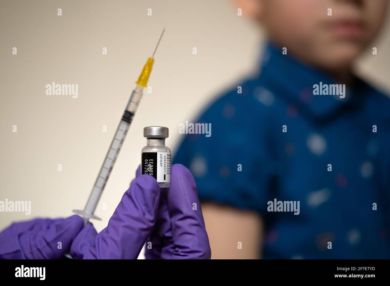Real authentic Pfizer-BioNTech vaccine vial hold in hand with syringe and child sitting with rolled up sleeve on the blurred background. Editorial illustrative. Staf Stock Photo