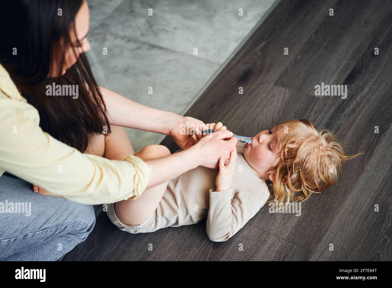 woman feeding baby food to her son, who is lying on the floor Stock Photo