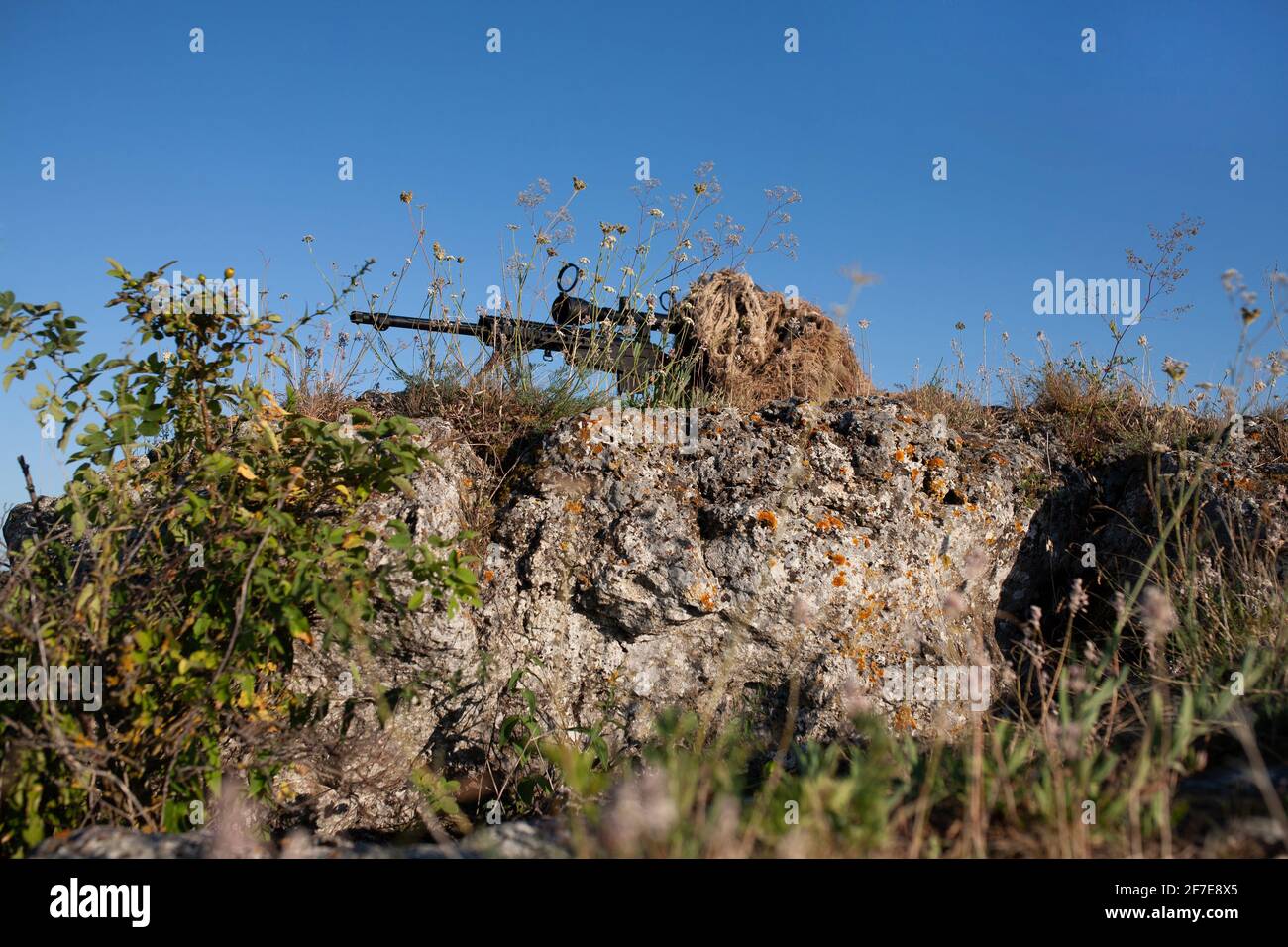 special operation forces sniper in ghillie (camouflage) suit with a high-precision rifle with optic scope in a combat position in the mountains Stock Photo