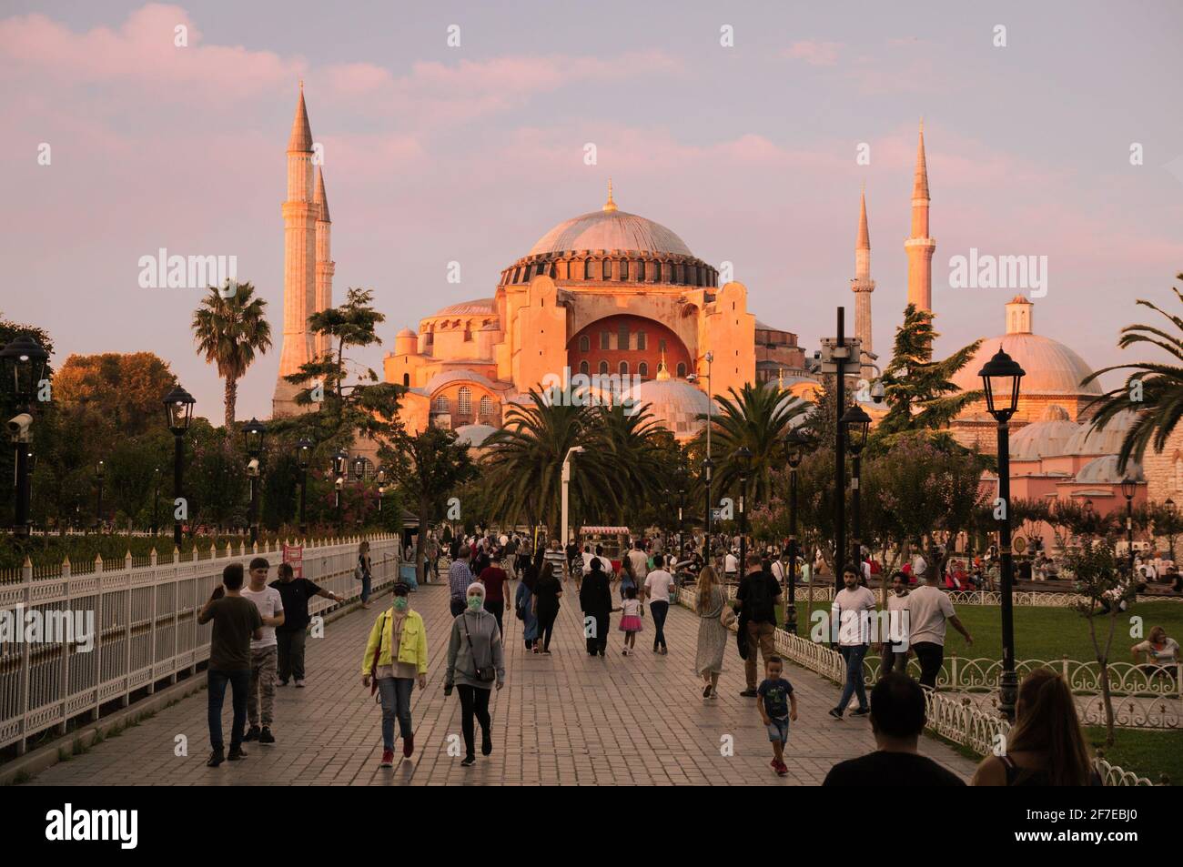 ISTANBUL, TURKEY - 09 07 2020: People walking in Sultan Ahmet Park in front of Hagia Sophia Cathedral Mosque Basilica lit with warm sunset sun rays in Stock Photo
