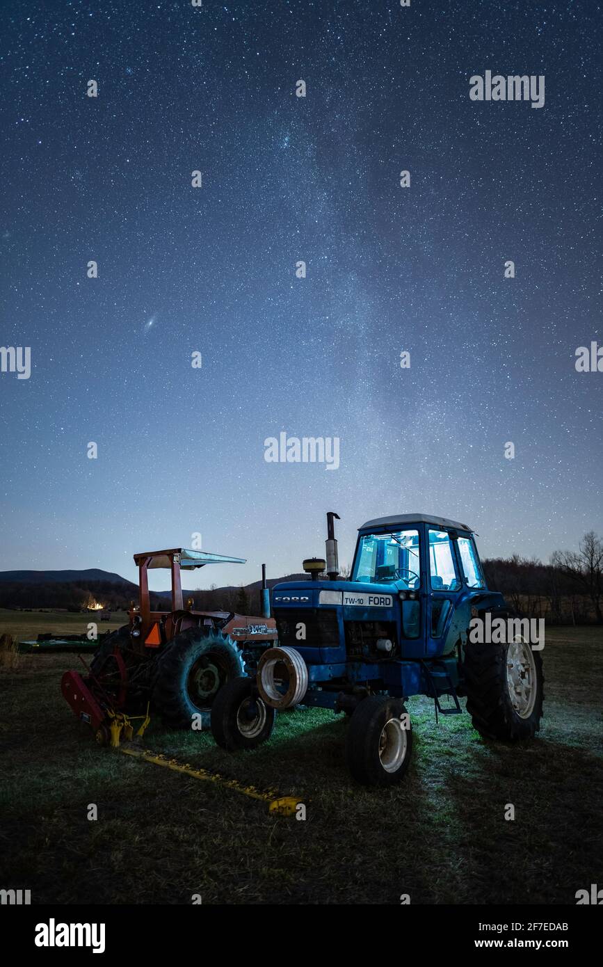 A Ford tractor glows as the Winter Milky Way shoots out up above on a Virginian farm. Stock Photo