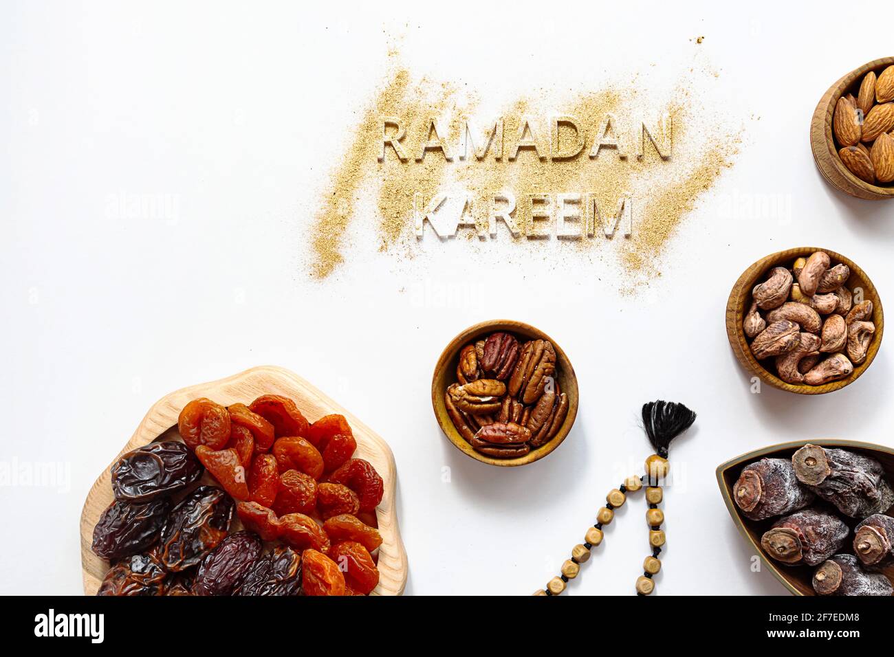'Ramadan Kareem' and muslim Iftar food, modern festive concept in gold and white colors. Ramadan Kareem with premium dates, nuts, dried fruits in wood Stock Photo